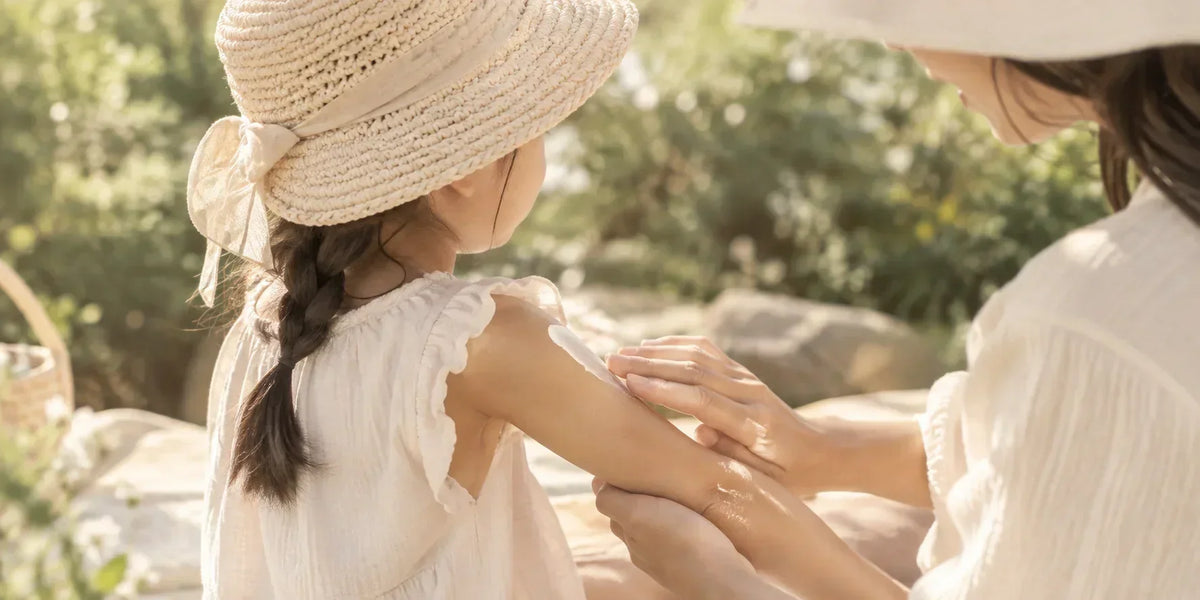 Child wearing a sun hat and receiving sunscreen outdoors