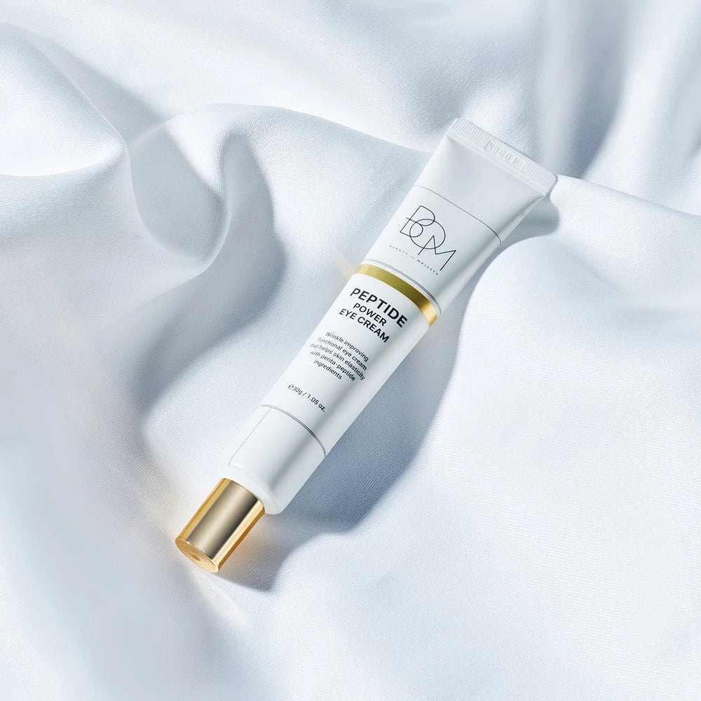 Un tube de crème contour des yeux BOM Peptide Power, avec un bouchon doré, posé sur un tissu blanc drapé