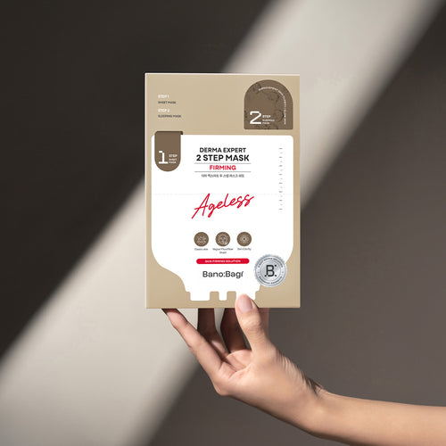 Hand holding a 'Bano Bagi Derma Expert 2 Step Mask Firming against a neutral background with a ray of light
