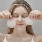 Woman holding two Equlib Eau Briller Glass Toning Pads near her face against a neutral background