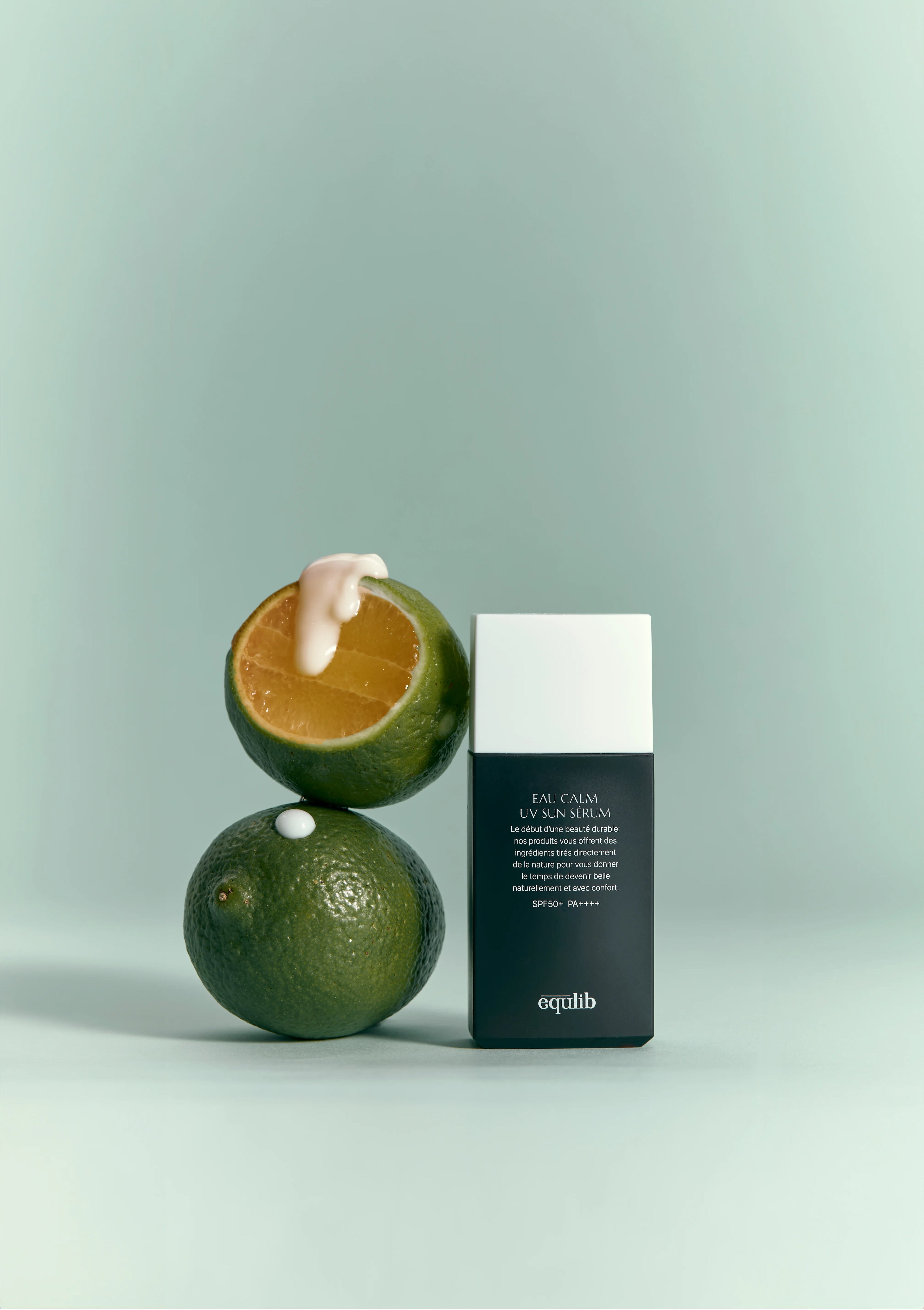 Two limes and a Equlib Eau Calm UV Serum SPF50+ PA++++ on a light green background