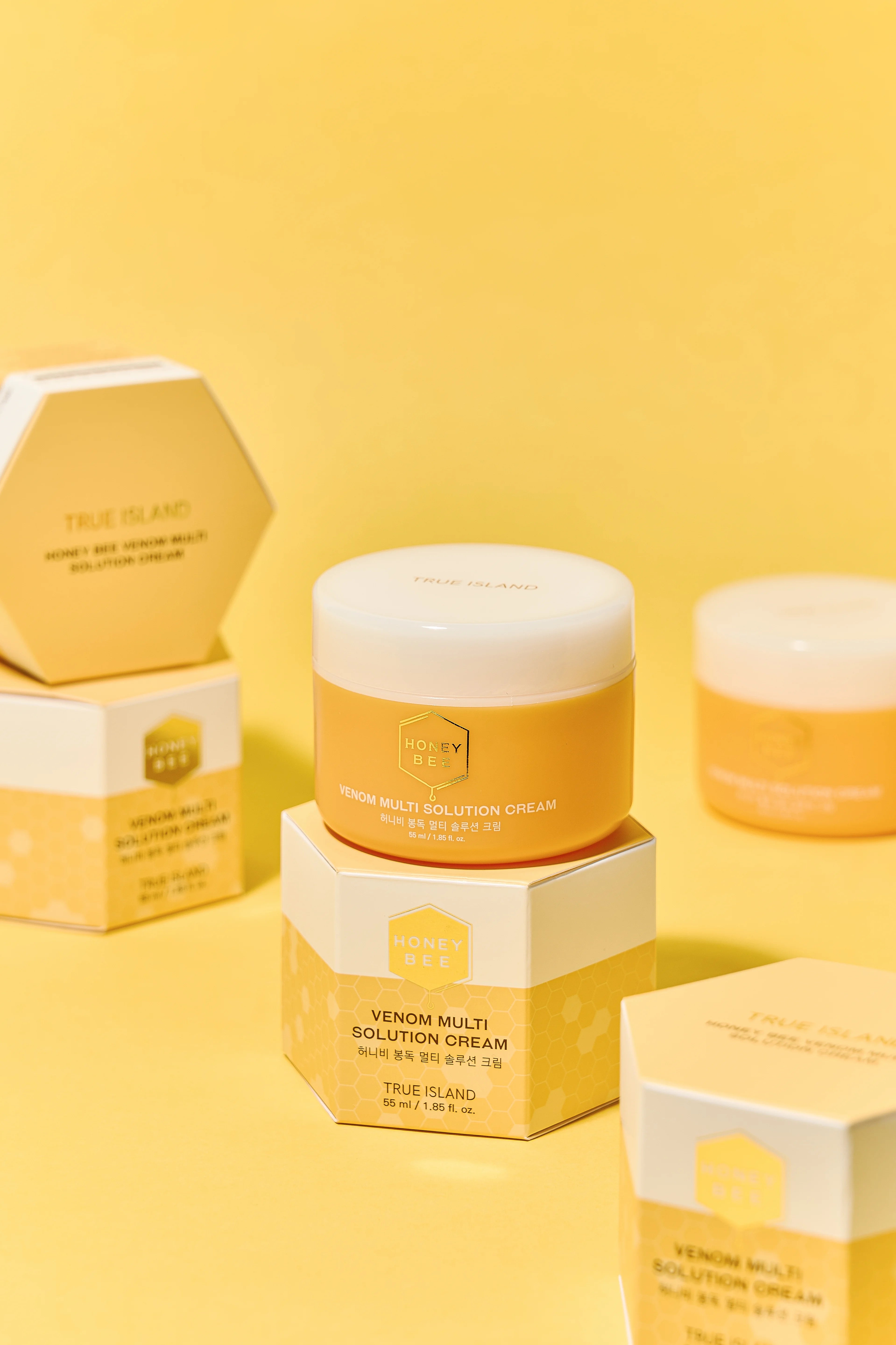 Honey Bee Venom Multi Solution Cream skincare products in yellow and white packaging, arranged on a solid yellow background