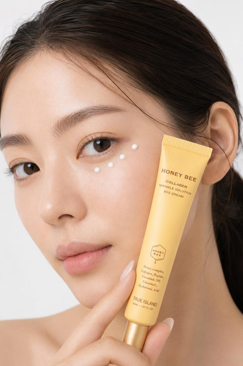 A close-up of a woman holding a yellow tube of True Island Honey Bee Collagen Eye Cream next to her cheek