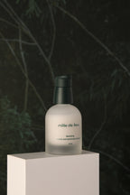 Mille de Fleur Blanche Extra Concentrate Sérum on a white platform with a dark green leafy background