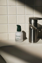 Bottle of Mille de Fleur Blanche Extra Concentrate Sérum on a bathroom counter with a tiled wall in the background