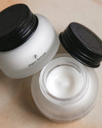 Two Mille de Fleur Blanche Repairing Crèmes on a beige background, one open showing cream inside