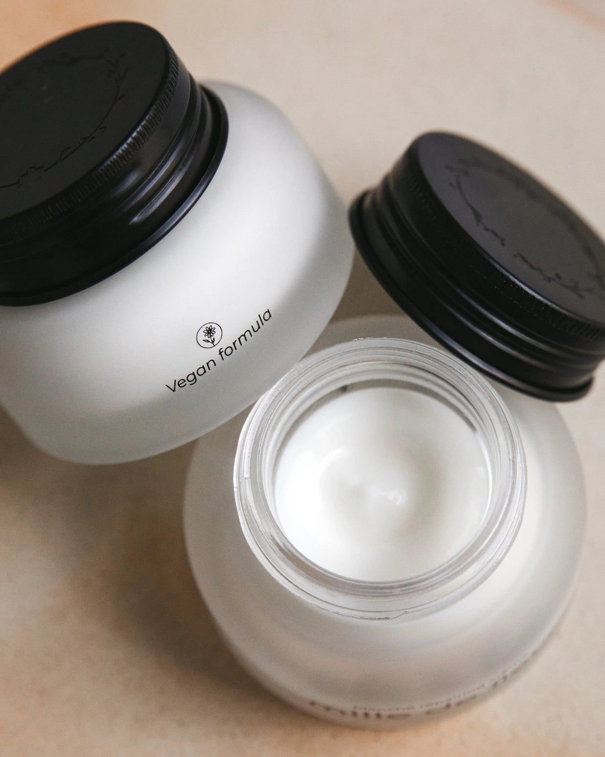 Two Mille de Fleur Blanche Repairing Crèmes on a beige background, one open showing cream inside
